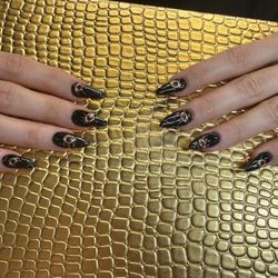 Naveana Nail Salon - Glossy black almond nails with ruby-inspired accents and luxe gold detailing