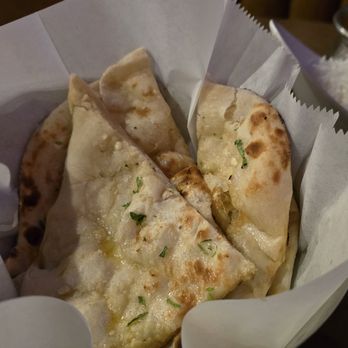 Monsoon Grill - Garlic Naan bread - A serving of garlic naan bread with chopped herbs is presented in a paper-lined basket, likely at an Indian restaurant. - Indian Near Me - Topeka, Kansas