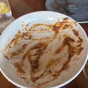PASTA - Clean plate club. - A large, empty pasta bowl with sauce streaks and remnants, placed on a wooden table at a restaurant. - Italian Near Me - Miami, Florida