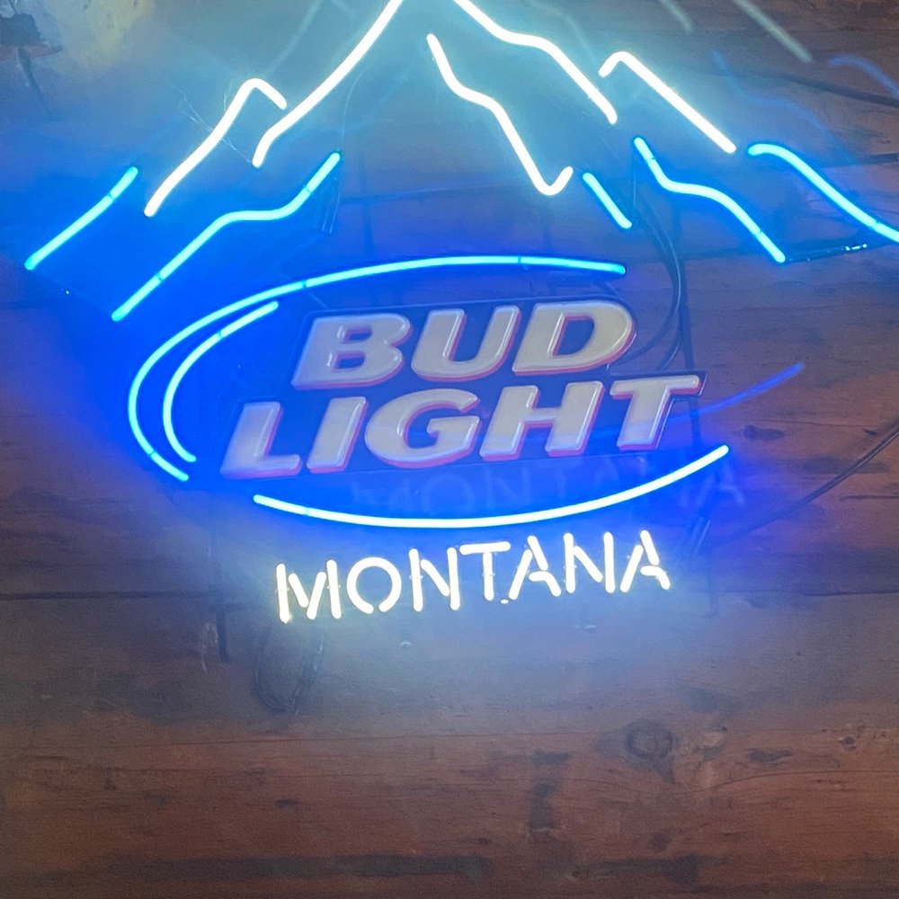 The Stillwater Bar - a blue neon sign with a mountain in the background - Bars Near Me - Olney, Montana