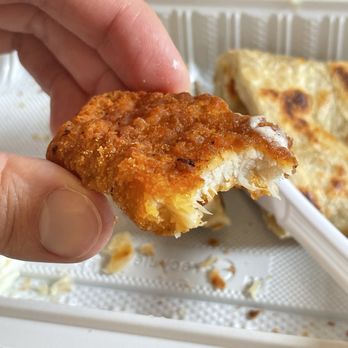 Dek Doi Cafe - Fried chicken and roti - A person holds a piece of fried chicken with a golden, crispy coating and visible white meat inside, with more fried chicken pieces in the background. - Cafes Near Me - Oakland, California