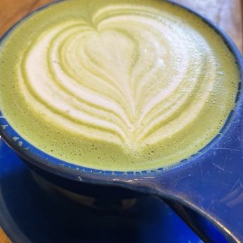 Philter - Matcha latte - A matcha latte with foam art in a blue ceramic cup, placed on a matching saucer on a wooden table. - Coffee & Tea Near Me - Kennett Square, Pennsylvania