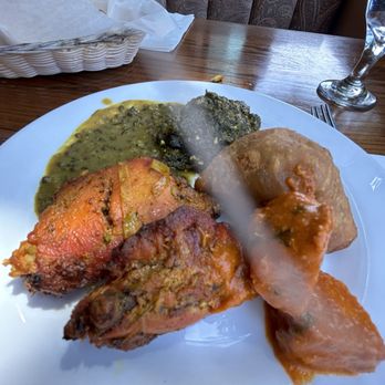 Masala - Marsala serving - A white plate contains Indian cuisine with various dishes such as chicken, spinach, and vegetable curry, served on a wooden table. The background includes a bread basket, a glass of water, and patterned curtains. The image captures a meal likely served at an Indian restaurant. - Indian Near Me - Somerville, Massachusetts