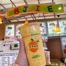 a person holding a drink in front of a fruit stand