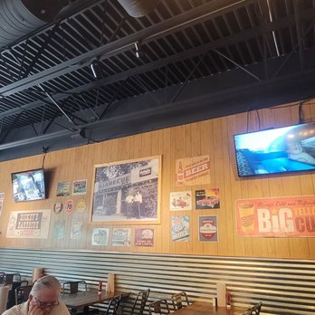 Dickey's Barbecue Pit - A restaurant interior featuring a wooden wall decorated with vintage signs and two mounted TVs, with tables and chairs arranged for dining. - Barbeque Near Me - Eagan, Minnesota