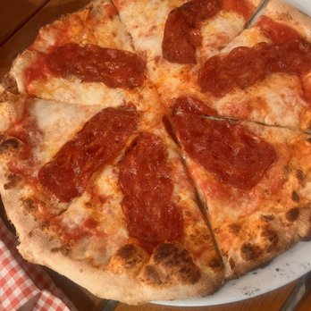 Spris Artisan Pizza - Lincoln Road - A pizza with a thin, crispy crust topped with melted cheese and slices of pepperoni, served on a white plate. The pizza is cut into slices, and the setting includes a wooden table with a glass of beverage nearby. - Pizza Near Me - Miami Beach, Florida
