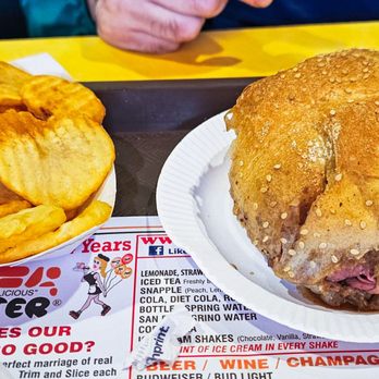 Roll-N-Roaster - Fries and roast beef - A crispy fried chicken sandwich with pink meat inside is served on a paper plate, accompanied by a bowl of potato chips on a tray. - American Near Me - Brooklyn, New York