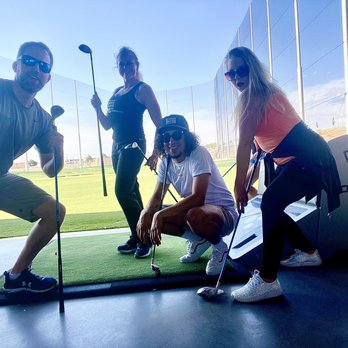 Topgolf - Team building - Four individuals are at Topgolf in Albuquerque, NM, holding golf clubs on a driving range with a netted enclosure and a clear sky. - New American Near Me - Albuquerque, New Mexico