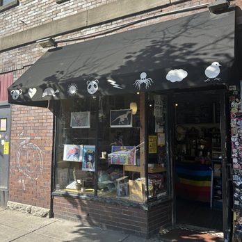 The Intersection Cafe - the outside of the store - A small shop with a black awning featuring white icons like a bear, octopus, cloud, and bird, with artwork displayed in the window. - Coffee & Tea Near Me - Buffalo, New York