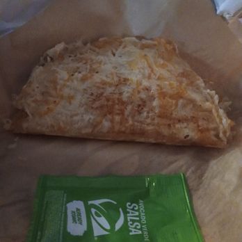 Taco Bell - Cantina Crispy Chicken Taco - A folded taco wrapped in foil is positioned on a piece of brown paper, with a green salsa packet labeled 'Avocado Verde Salsa' placed in front. The taco appears to contain cheese and possibly other ingredients, and the setting suggests it is from Taco Bell in Espanola, NM. - Fast Food Near Me - Espanola, New Mexico