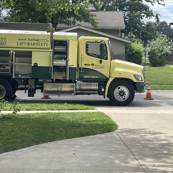 Bartlett Tree Experts - A yellow and green Bartlett Tree Experts service truck is parked on a suburban street, with traffic cones placed around it, and residential houses in the background. - Tree Services Near Me - Bedford, Ohio