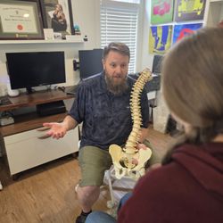 Dr. Spencer Devenney, educated a patient about Spine pain holding a model spine, in Chilliwack BC.