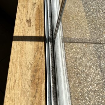 Everclean Services - Before - A window track with visible dirt and dust accumulation, adjacent to a wooden surface and a concrete sidewalk outside. - Home Cleaning Near Me - Pasadena, California