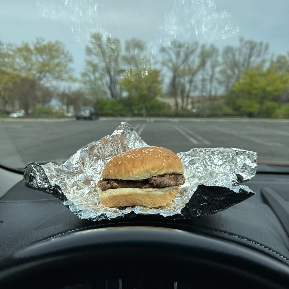 a hamburger on tin foil on the dashboard of a car