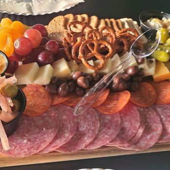 Ethos Craft Brewing - Small charcuterie board!! Sooo delicious!! - A charcuterie board features sliced cured meats, cheeses, grapes, orange slices, pretzels, and pickles, arranged on a wooden serving board. - Breweries Near Me - Cullman, Alabama
