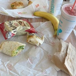 Two smoothies, a hummus wrap with chips, and a Santa fruit chicken wrap with banana.