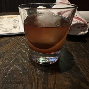 Roosters - Old Fashioned - A glass of Old Fashioned cocktail with ice is placed on a dark wooden table, with a menu and a rolled napkin in the background. - Chicken Wings Near Me - Glenside, Pennsylvania