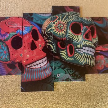 Metate - Decorations - Two decorative skull masks with intricate floral and geometric patterns are placed on a textured gold surface. The masks feature bright colors, including red, green, and black, with detailed designs around the eye sockets and forehead. The masks are positioned side by side, with one slightly overlapping the other, and the background includes additional colorful elements. The image emphasizes the artistic craftsmanship and vivid color palette of the masks. - Mexican Near Me - Bronx, New York