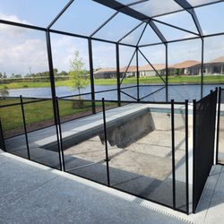 The Pool Fence Company - 4' black mesh pool fence with 90° turn, installed around an empty pool inside a screened enclosure with a scenic lake view in the background