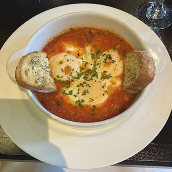 Il Piatto - Italian shakshuka - A dish of Italian shakshuka with eggs in tomato sauce, garnished with herbs, accompanied by slices of bread, served on a white plate. - Italian Near Me - Washington, DC, District of Columbia