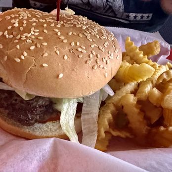 Babe's Blue Room - Delicious burger. - A cheeseburger with lettuce, tomato, and a beef patty inside a sesame seed bun is placed on a tray lined with pink paper. Next to the burger, there is a serving of crinkle-cut fries. The tray appears to be part of a casual dining setting, possibly at a diner or fast-food restaurant. - Bars Near Me - Ormond Beach, Florida