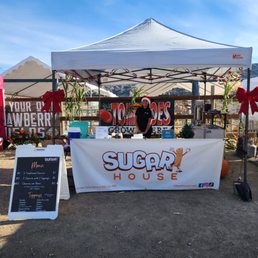 a woman standing behind a sugar house sign a woman standing behind a sugar house sign