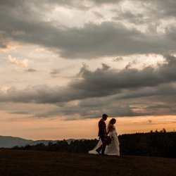 Serenity Ridge - A bride and groom post-wedding, walking across the lawn at sunset.