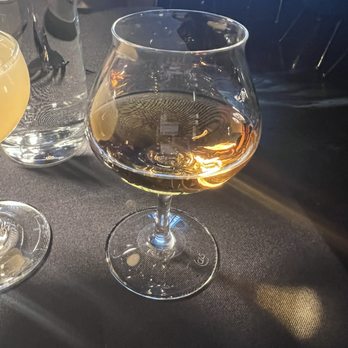 Flavorture - UncleNearest whiskey - A snifter glass filled with whiskey is placed on a black table, with a water pitcher and another glass partially visible nearby. - Bars Near Me - Washington, DC, District of Columbia