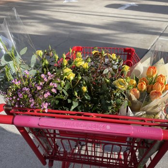 Trader Joe's - A red shopping cart contains multiple flower bouquets, including yellow roses and purple flowers, in a parking lot. - Grocery Near Me - Katy, Texas