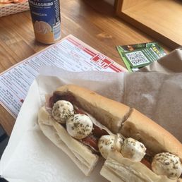 A sandwich featuring mozzarella balls, tomato slices, and herbs on a baguette, placed on a paper wrapper on a wooden table.