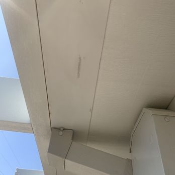 Sunstate Landscape - The image depicts the corner of a white building's exterior, including siding and trim components. Visible are dirt marks and a small area of damage or wear on the trim. The background shows a clear sky and some power lines, indicating an outdoor setting. - Masonry/Concrete Near Me - Riverside, California
