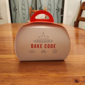Chatime - A bakery box with "Bake Code" branding and illustrations of baked goods, placed on a wooden table in a home setting. - Bubble Tea Near Me - Toronto, Ontario