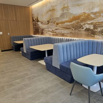 For Five Coffee Roasters - Seating area - The image shows a modern cafe interior with booth seating arranged along a textured wall featuring a landscape mural in neutral tones. The booths have blue velvet upholstery with vertical stitching, and each has a light-colored wooden table. The floor is covered with large gray tiles, and the ceiling has recessed lighting. The overall design emphasizes a clean, minimalist aesthetic with natural materials and subtle lighting accents. - Coffee Roasteries Near Me - Washington, DC, District of Columbia