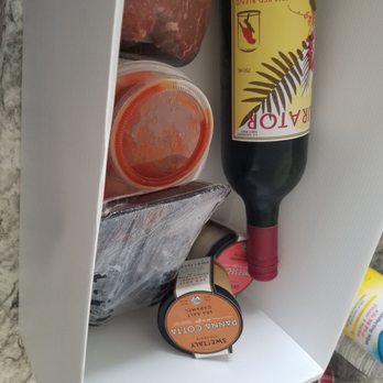 Empire Fish - 2 tenderloins, 2 lobster tails, shrimp cocktail, 2 desserts in a jar and a red blend - The image shows the interior of a refrigerator door with several food and beverage items. There is a piece of raw salmon, a plastic container with a red sauce, a package of scallops labeled SWETAIL PANNY COTTA, a bottle of red wine, and a small container of butter. The items are arranged vertically along the door, with a white interior background. - Seafood Markets Near Me - Milwaukee, Wisconsin