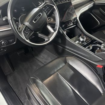 Auto Envy Detailing - The image depicts the interior of a Jeep vehicle, including the steering wheel, dashboard with a touchscreen display, and a black leather front seat. - Auto Detailing Near Me - Hudson , New Hampshire