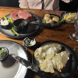 Prime Rib - A dining table features prime rib, mashed potatoes, and side dishes, including asparagus and breaded cheese, served on black plates.