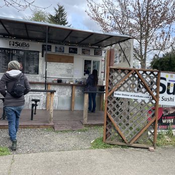 Subo Sushi Burritos - Order area - A small food stand for Subo Sushi Burritos is set up outdoors with two customers placing orders. The stand has a menu and a sign for online orders. - Sushi Bars Near Me - Eugene, Oregon