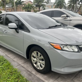 Fixbodycar - New paint work - A silver Honda sedan with tinted windows is parked on a concrete driveway in a residential neighborhood, with a gray SUV parked behind it. - Body Shops Near Me