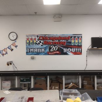 Chicagoland Raceway - yep - The image shows a wall at Chicagoland Raceway with a clock, a banner celebrating the 20th anniversary, a small TV, and storage shelves with boxes. - Hobby Shops Near Me - Westmont, Illinois