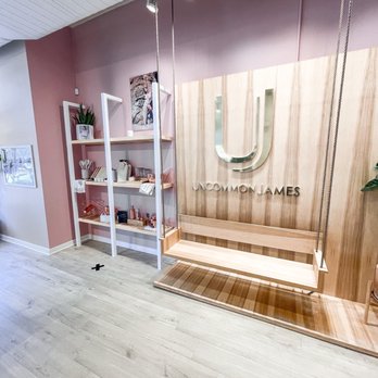 Uncommon James - The image shows the interior of Uncommon James, featuring a wooden wall with the logo and name, and white shelving with decorative items. - Accessories Near Me - Chicago, Illinois