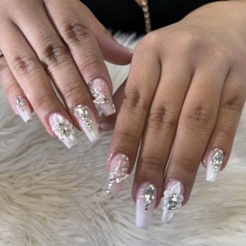 Flashy Nails - My nails! - Hands with elaborately decorated acrylic nails, featuring floral patterns, rhinestones, and a white and pink color scheme, resting on a furry surface. - Nail Salons Near Me - Albuquerque, New Mexico