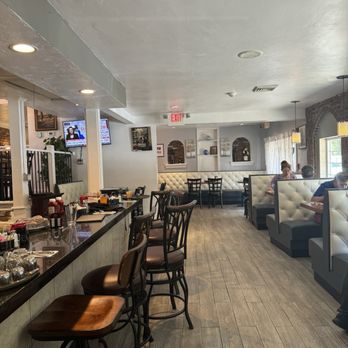 185 Bistro - A restaurant interior featuring booths along the window, a bar with chairs, and a few customers dining. The decor includes brick walls, curtains, and wall-mounted TVs. - Breakfast & Brunch Near Me - Worcester, Massachusetts