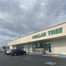 Dollar tree next to post office - The image depicts a Dollar Tree retail store with a large sign on the building's facade. The parking lot in front includes several parked cars and designated accessible parking spaces marked with blue and white signs. The sky above is filled with gray clouds, indicating overcast weather. The storefront features glass doors and windows, with some visible signage inside.