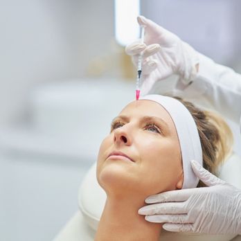 Ageless Beauty Center - A professional is administering an injection into a woman's forehead as she lies on a white bed with her head elevated... - Medical Spas Near Me - Okemos, Michigan Ageless Beauty Center - A professional is administering an injection into a woman's forehead as she lies on a white bed with her head elevated... - Medical Spas Near Me - Okemos, Michigan