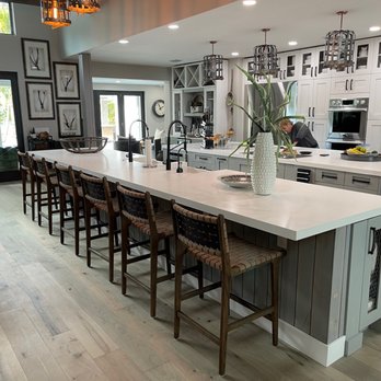 Zimmerman Kitchen Design - My dream kitchen - A spacious kitchen features a large island with bar stools, white cabinets, and pendant lighting, with a person working at the counter. - Kitchen & Bath Near Me - Boca Raton, Florida