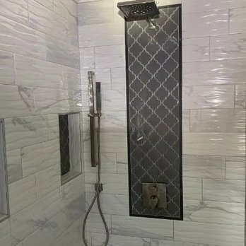 SHARP Improvements - A modern shower with light gray marble-patterned tiles, a decorative dark gray accent tile strip, and brushed nickel fixtures. - Plumbing Near Me - Monroe, Georgia SHARP Improvements - A modern shower with light gray marble-patterned tiles, a decorative dark gray accent tile strip, and brushed nickel fixtures. - Plumbing Near Me - Monroe, Georgia