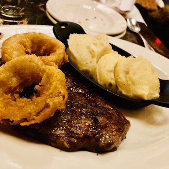 Grand Lux Cafe - Rib Eye Steak Served with Potato and onion rings - American Near Me - Paramus, New Jersey Grand Lux Cafe - Rib Eye Steak Served with Potato and onion rings - American Near Me - Paramus, New Jersey
