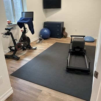 Simply Floors & Painting - Basement LVP floors - A small home gym features a stationary bike, a treadmill, a stability ball, and a TV mounted on the wall, with a window providing natural light. - Flooring Near Me - Centennial, Colorado