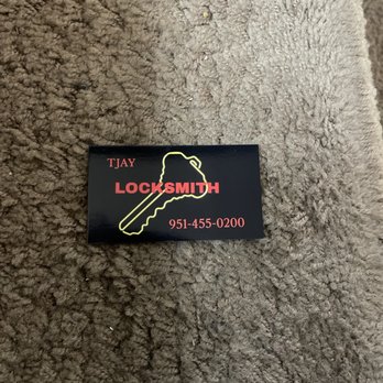 TJay Locksmith - Business card.. - The image shows a black rectangular business card for TJay Locksmith, with a yellow outline of a key graphic. The card has red text displaying the business name, contact number, and the word 'LOCKSMITH'. It is positioned on a textured, brown, carpet-like surface. The design emphasizes locksmith services and contact information. - Keys & Locksmiths Near Me
