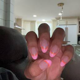 Acyrlic nails from "De Paris Nails" - A hand with a pink and orange French manicure is held up in a living room, with a kitchen visible in the background.